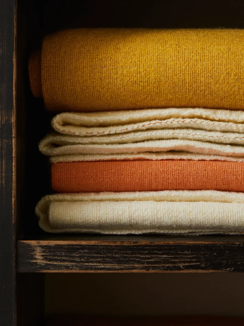 Pila di coperte in cotone intrecciato nei toni senape, ruggine e crema su una mensola